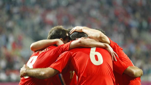 Mehrere Fußballspieler in roten Trikots umarmen sich auf dem Spielfeld.