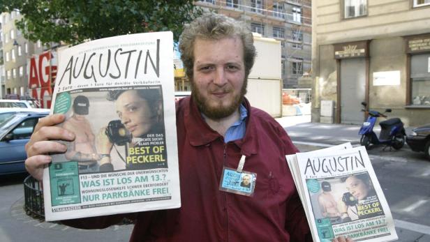 Ein Mann hält zwei Ausgaben der Wiener Straßenzeitung „Augustin“ in die Kamera.