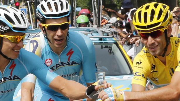 Radrennfahrer der Mannschaft Astana stoßen mit Sekt während eines Rennens an.