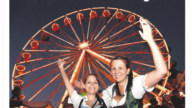 Zwei Frauen in Dirndln posieren vor einem beleuchteten Riesenrad auf einem Volksfest.