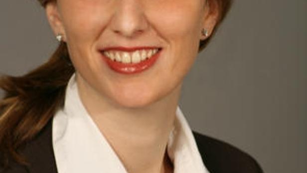 Eine lächelnde Frau in einem dunklen Blazer und einer weißen Bluse.