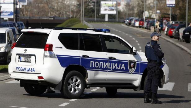 Ein Polizist steht neben einem serbischen Polizeiauto.