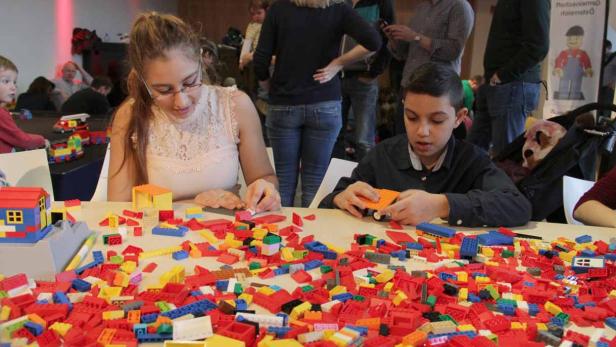 Eine Frau und ein Junge sitzen an einem Tisch voller Legosteine und bauen.
