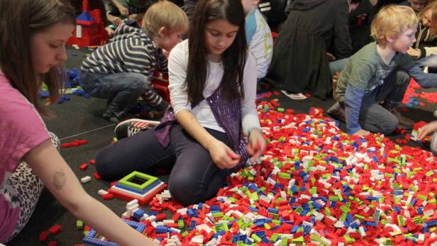 Eine Gruppe von Kindern sitzt auf dem Boden und spielt mit vielen bunten Legosteinen.