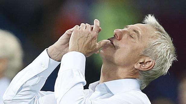 Ein Mann im weißen Hemd führt eine Geste mit seinen Fingern an seinem Mund aus.