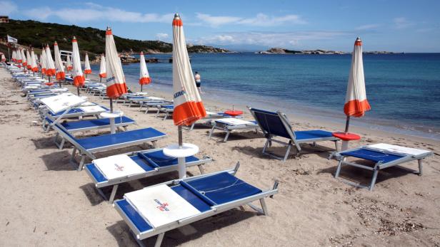 Viele Liegestühle und Sonnenschirme stehen an einem Strand bereit.