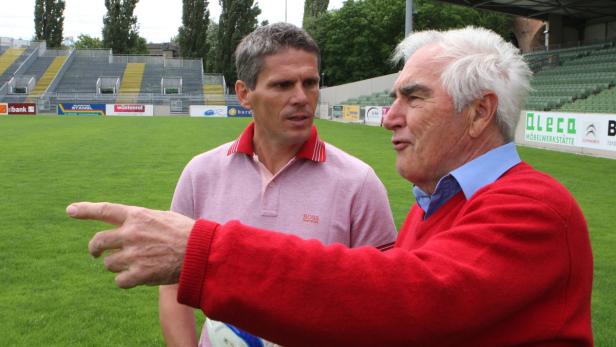 Zwei Männer unterhalten sich auf dem Rasen eines Fußballstadions.