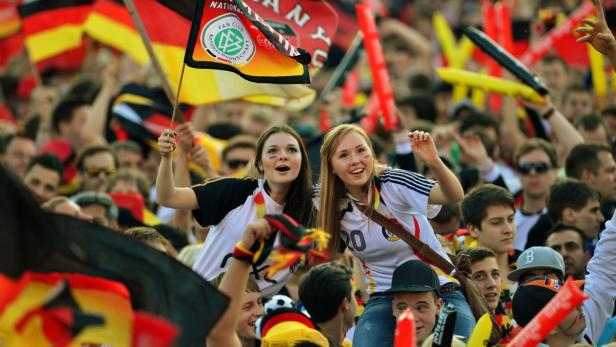 Zwei junge Frauen feiern mit Deutschland-Flaggen in einer Menschenmenge.