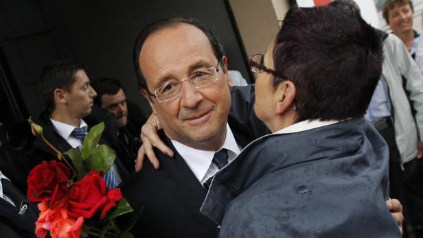 François Hollande umarmt eine Frau und hält einen Strauß roter Rosen.