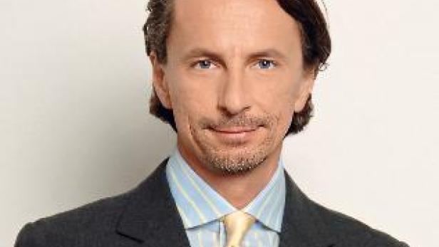 Ein Mann mit braunen Haaren und einem grauen Anzug blickt in die Kamera.