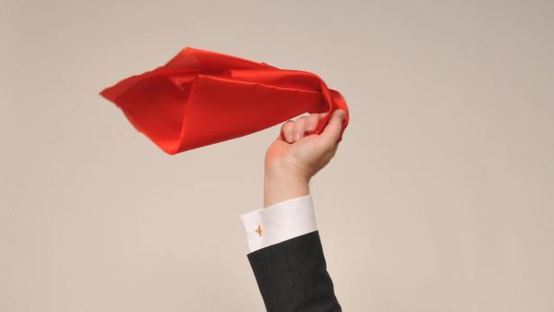 Eine Hand in einem Anzug hält ein rotes Tuch hoch.