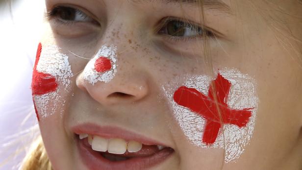 Ein Mädchen mit aufgemaltem englischen Kreuz auf der Wange lächelt.