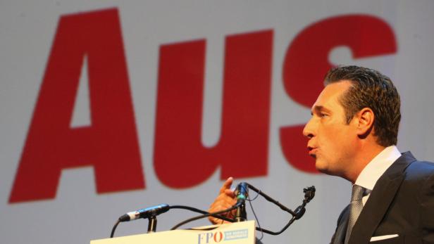 Ein Mann in Anzug spricht vor einem roten Schriftzug „Aus“.