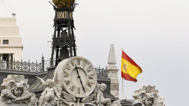 Detailaufnahme des Banco de España Gebäudes mit Uhr und spanischer Flagge.