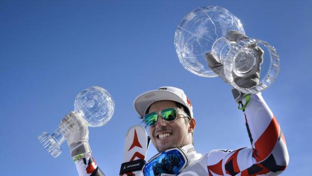 Ein Skirennläufer hält zwei Kristallkugeln in die Höhe.