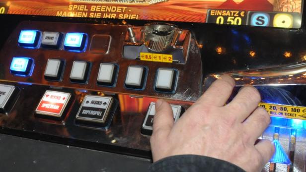 Eine Hand bedient einen Spielautomaten mit verschiedenen Knöpfen und Anzeigen.