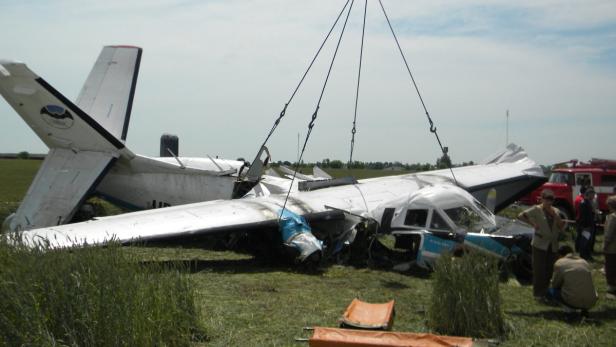 Ein beschädigtes Kleinflugzeug liegt auf einem Feld, während es von einem Kran angehoben wird.