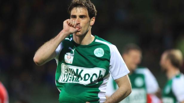 Ein Fußballspieler im grün-weißen Trikot jubelt mit dem Finger am Mund.