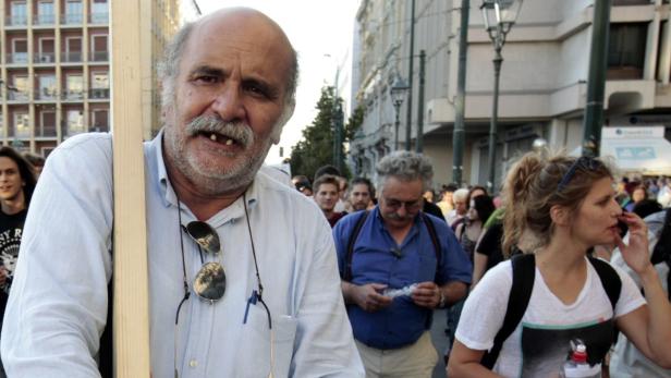 Ein Mann mit Schnurrbart steht bei einer Demonstration in einer Menschenmenge.