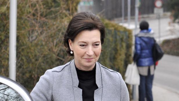 Eine Frau mit dunklen Haaren und einem grauen Blazer lächelt.