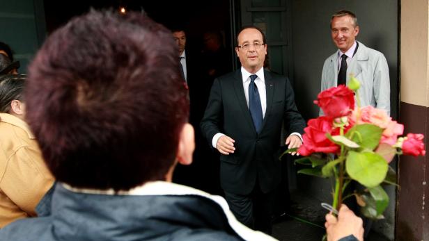 François Hollande wird von einer Person mit einem Rosenstrauß begrüßt.