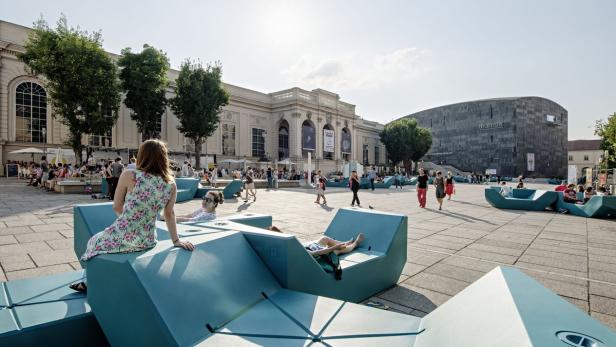 Menschen entspannen auf blauen Sitzgelegenheiten im Museumsquartier in Wien.