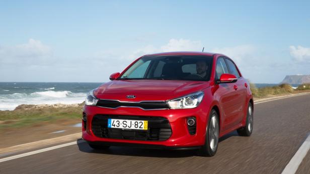 Ein roter Kia Rio fährt auf einer Küstenstraße.