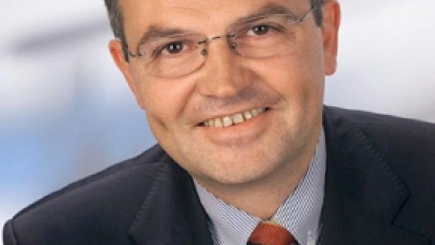 Ein lächelnder Mann mit Brille, Anzug und Krawatte.