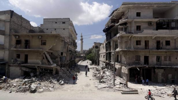 Zerstörte Gebäude säumen eine Straße mit Trümmern und einigen Passanten.