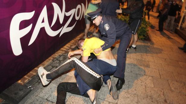 Ein Polizist greift einen Mann vor dem Hintergrund einer „Fanzone“-Werbung auf.