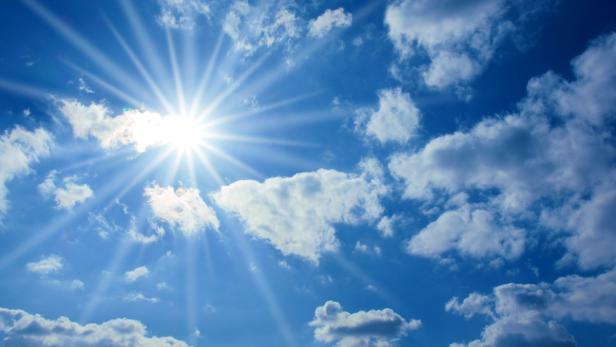 Die Sonne scheint hell durch die Wolken am blauen Himmel.