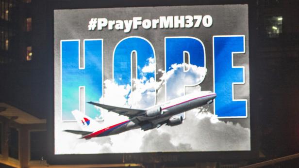 Eine Gedenktafel mit der Aufschrift „#PrayForMH370“ und dem Wort „HOPE“ mit einem Flugzeug im Hintergrund.