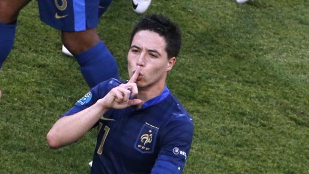 Ein französischer Fußballspieler in blauem Trikot mit dem Finger am Mund, um Ruhe zu signalisieren.