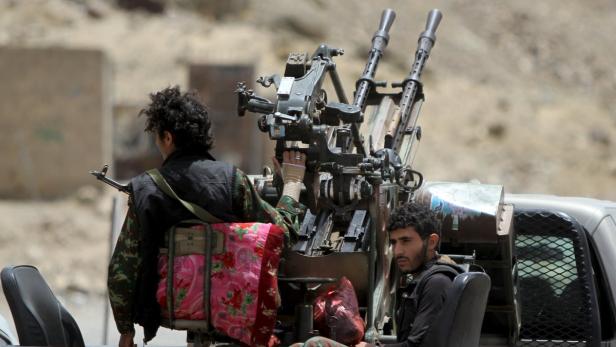 Zwei bewaffnete Männer sitzen auf der Ladefläche eines Pickups mit einem montierten Maschinengewehr.