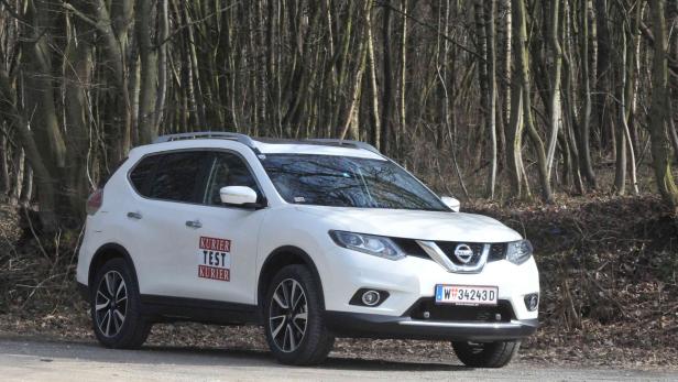 Ein weißer Nissan X-Trail steht auf einem Feldweg vor einem Wald.