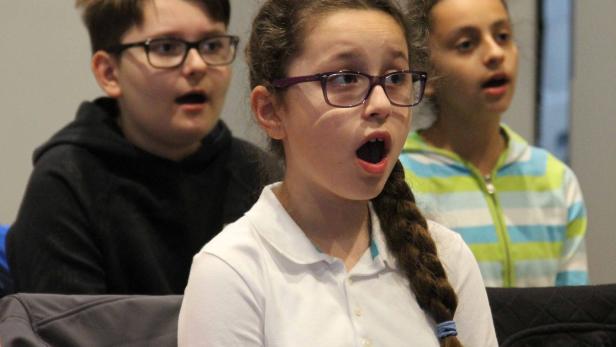 Drei Kinder mit offenem Mund, möglicherweise bei einem Chorauftritt.
