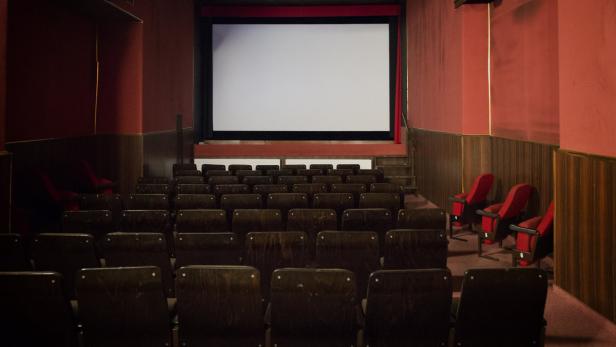 Blick auf eine leere Kinovorstellung mit roten Wänden und dunklen Holzstühlen.