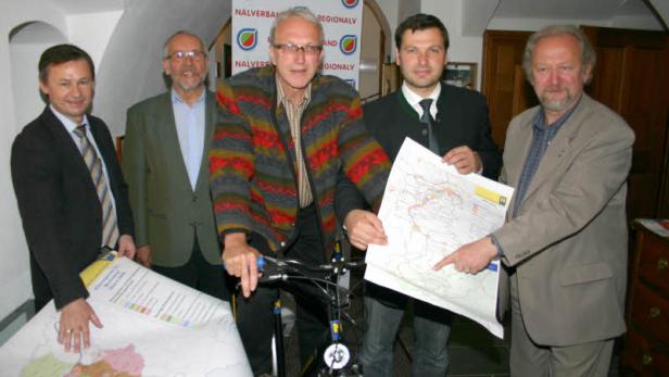 Eine Gruppe von Männern präsentiert Karten, einer sitzt auf einem Fahrrad.