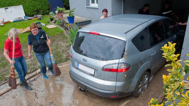 Zwei Frauen kehren Schlamm vor einem Haus und einem beschädigten Auto.