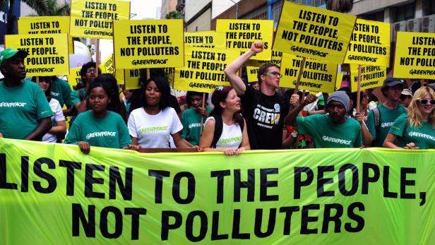 Eine Gruppe von Greenpeace-Aktivisten demonstriert mit Schildern und einem Banner.