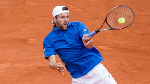 Ein Tennisspieler schlägt einen Ball auf einem Sandplatz.