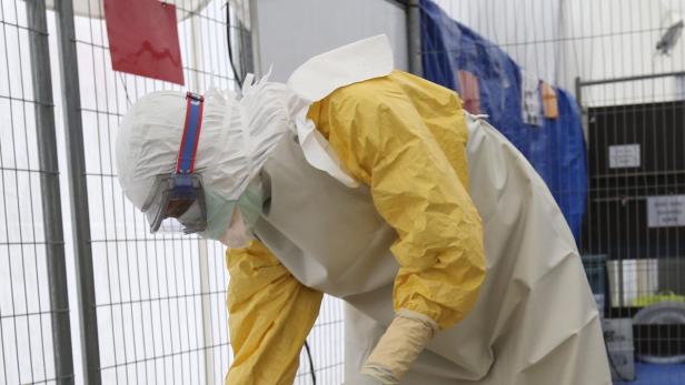 Eine Person in Schutzkleidung beugt sich in einem Zelt nach vorne.