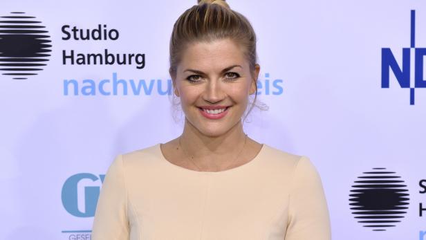 Eine lächelnde Frau mit blonden Haaren vor einem Veranstaltungsbanner.