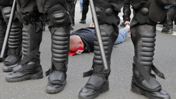 Ein Mann liegt auf dem Boden, umringt von Polizisten in Schutzausrüstung.