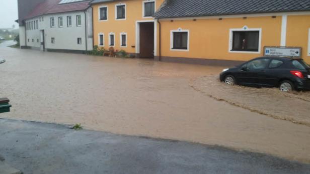 Ein schwarzes Auto fährt durch eine überflutete Straße in einem Wohngebiet.