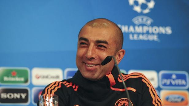 Ein lächelnder Mann mit Mikrofon vor einem Champions-League-Hintergrund.