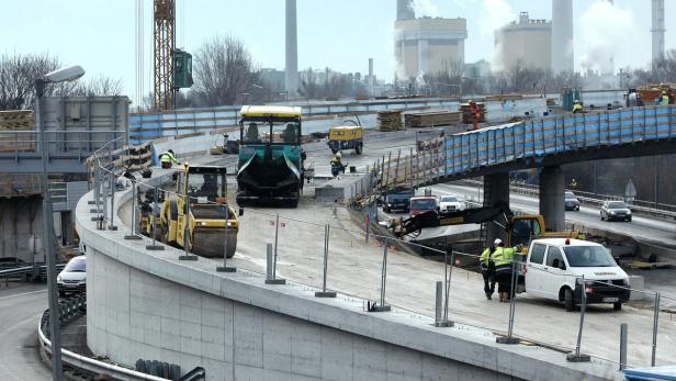 Bauarbeiten an einer Autobahnbrücke mit verschiedenen Baufahrzeugen und Arbeitern.