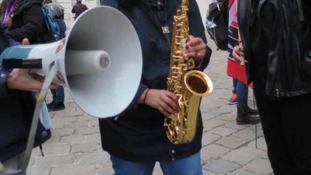 Eine Frau spielt Saxophon bei einer Demonstration, während eine andere Frau daneben steht.