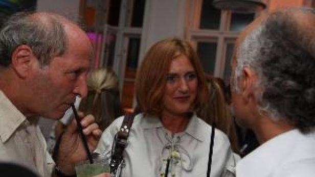 Drei Personen unterhalten sich auf einer Party, zwei trinken Cocktails.