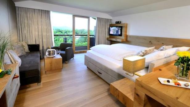 Ein helles Hotelzimmer mit Doppelbett, Sitzecke und Balkon mit Blick ins Grüne.